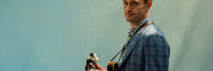 Der Musiker Chris Thieme mit Gitarre vor einem Stoff